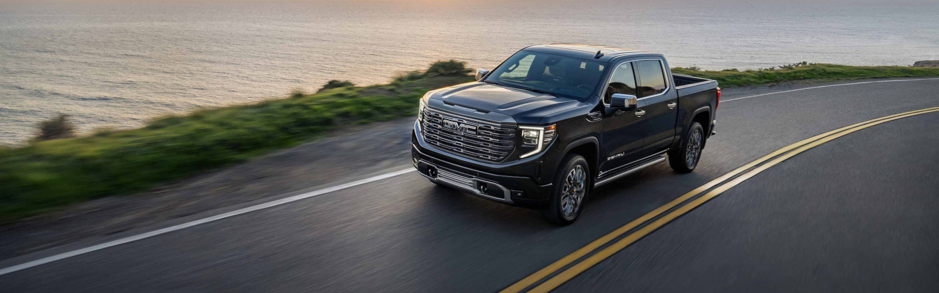 GMC Hummer EV Pickup driving along a coastal highway, showcasing rugged on-road performance with ocean views in the background