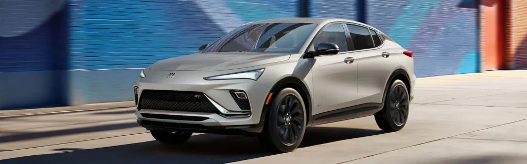 This image shows a front view of the 2026 Buick Envista SUV, driving past a vibrant mural with a sleek, modern design and dark rims.
