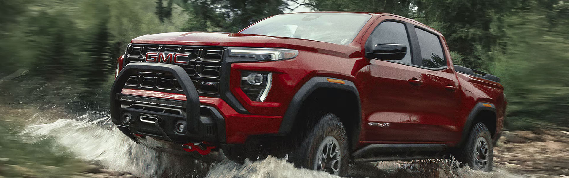 2026 GMC Canyon AT4X driving through a muddy terrain, splashing water.